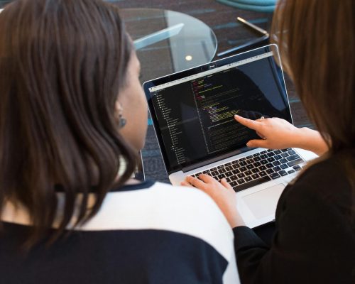 Two women working together on software programming indoors, focusing on code.