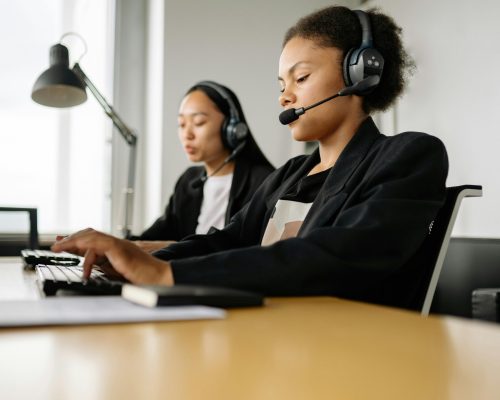 Two call center agents working at desks in an office setting with headsets.